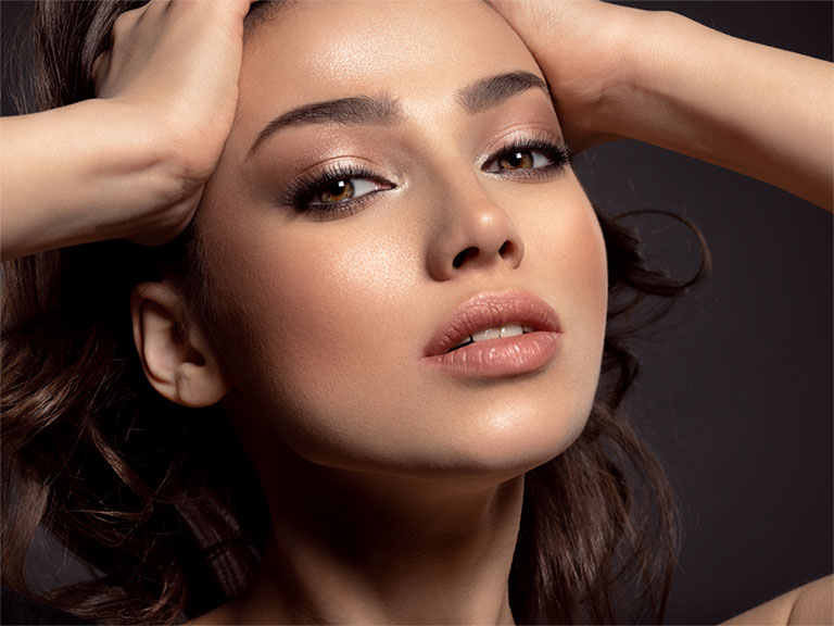 Elegant woman with youthful appearance looking sultry at the camera with her hands to either side of her forhead.